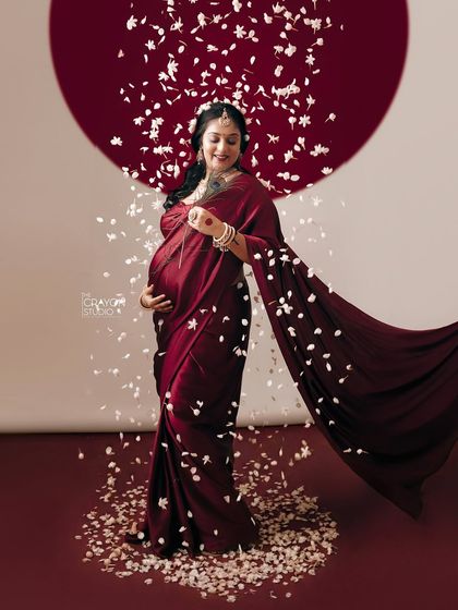 This is a duplicate of image 16, showing the full length portrait with the flowing red saree and petals, capturing the grace and power of the mother to be.