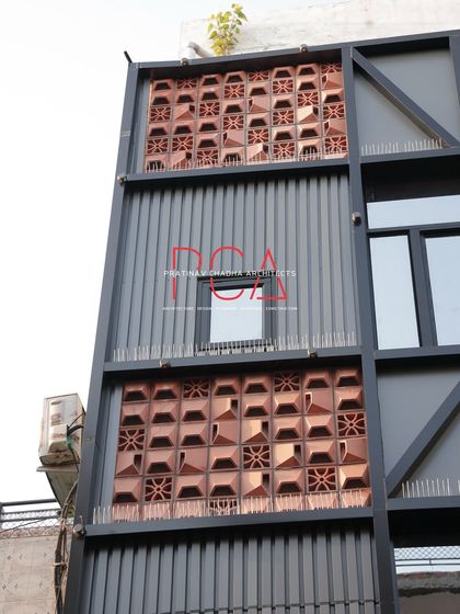 A close-up of the terracotta jaalis and corrugated ACP cladding on the Chadha Properties office. This image details the textural contrast that gives the facade its unique character.