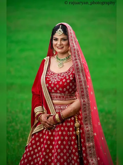 A classic bridal portrait of a bride in a stunning red lehenga, set against a vibrant green backdrop. I focused on creating a timeless image that highlights her elegance and the rich details of her wedding attire.