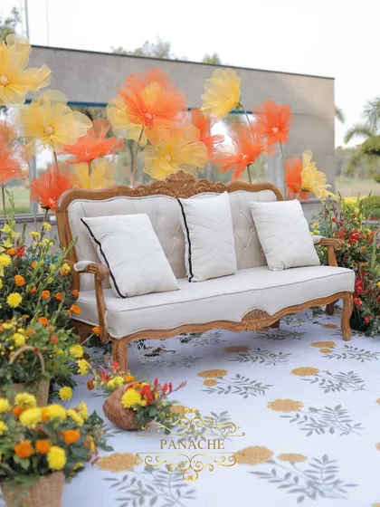 The main seating for the couple, featuring an elegant sofa against a backdrop of oversized organza flowers in shades of yellow and orange.