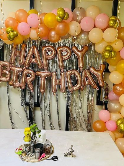 A simple and elegant 50th birthday setup at home. The decor features a rose gold and peach balloon arch over a shimmer curtain, with "Happy Birthday" and "50" foil balloons.