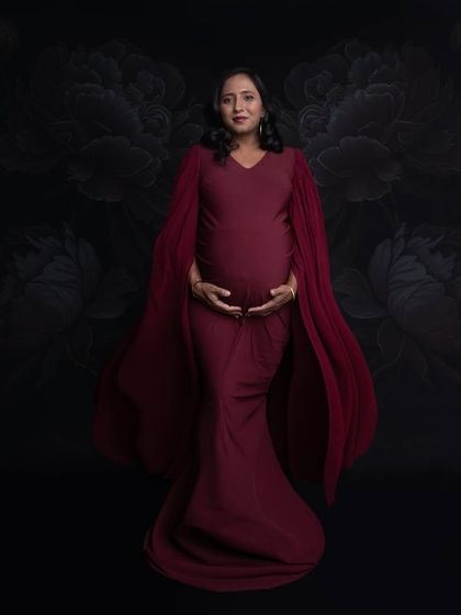 A classic and elegant portrait in a deep red gown with cape-like sleeves. The dark floral backdrop adds a touch of moody sophistication to the shot.