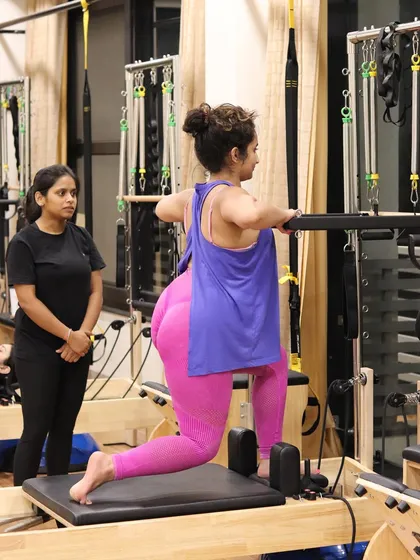 An instructor observes a client's form during a lunge on the Reformer. This constant supervision helps make immediate corrections, leading to better results and a safer workout experience.