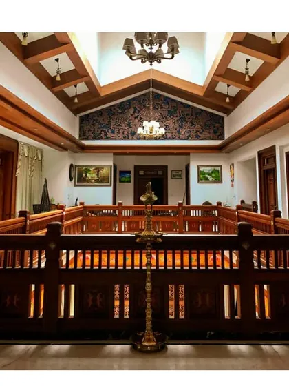 A view into a modern nalukettu, the traditional open courtyard that brings light and life into the core of a Kerala home. The design features ornate wooden railings and a double-height ceiling, blending heritage with contemporary scale.
