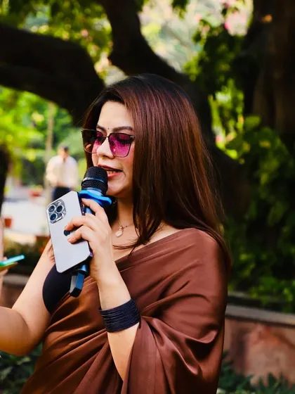 A close-up shot while hosting an outdoor event. The satin saree and sunglasses give it a chic, modern vibe.