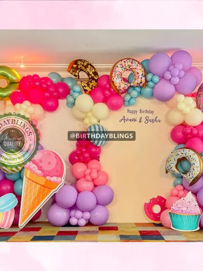 A "sweet treats" party with donuts, ice cream, and macarons. The colorful balloon arch and large food cutouts are fun and appetizing.