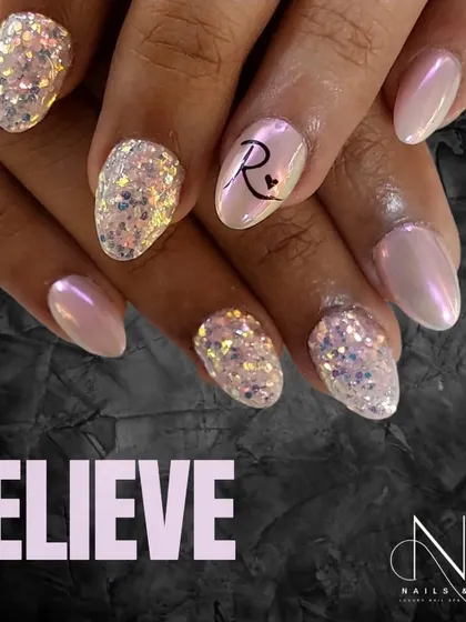 A personalized and pretty design. This look combines a pearlescent pink polish, chunky iridescent glitter, and a custom initial on the ring finger.
