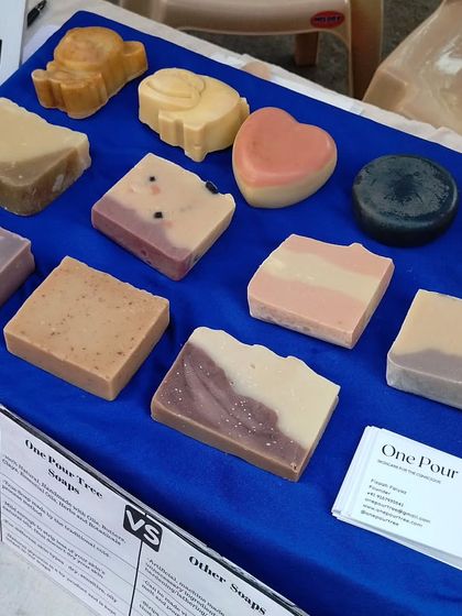 A display of my diverse soap collection at a local market. You can see various shapes, sizes, and natural colorants, from the heart-shaped 'Juliet' to the dark Activated Charcoal soap and fun animal shapes for kids.