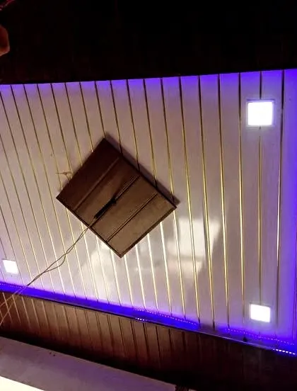 A PVC panel ceiling with a central wood-finish diamond shape. The purple backlighting and square spotlights create a sleek and modern aesthetic.