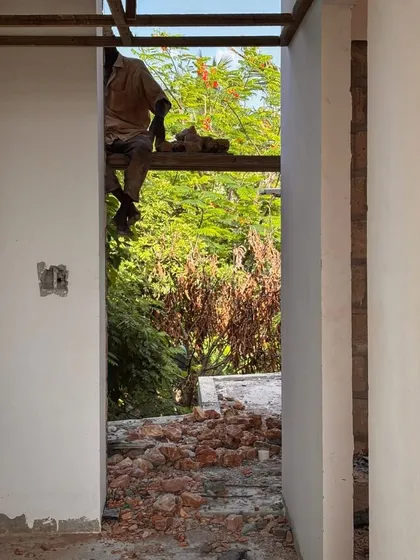 A worker sits on a scaffold plank inside an unfinished room at Kizikula. The simple opening provides a framed view of the lush greenery outside, a key element of the design.