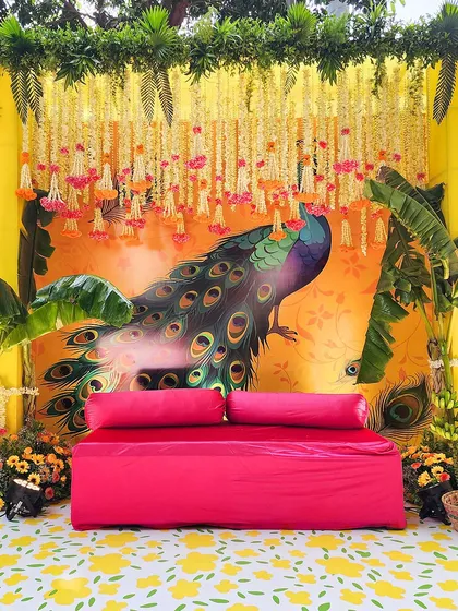 Our thematic decor brings stories to life. This vibrant Mehendi seating features a beautiful hand-painted peacock backdrop, a fuschia sofa, and traditional floral strings for a festive feel.