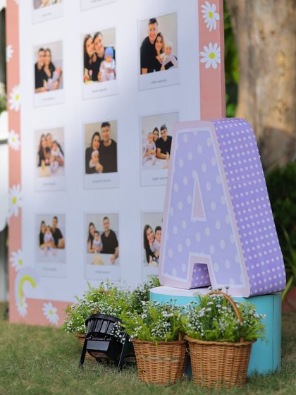 A close-up of the milestone board corner, featuring a large polka-dotted letter 'A' and baskets of fresh flowers, adding to the rustic charm of the outdoor setup.