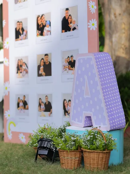 A close-up of the milestone board corner, featuring a large polka-dotted letter 'A' and baskets of fresh flowers, adding to the rustic charm of the outdoor setup.