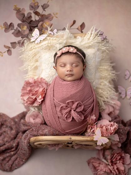 A beautiful newborn surrounded by butterflies and soft pink flowers. This setup creates a magical and whimsical portrait.