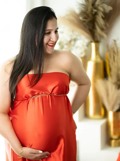 A candid and happy moment. This mom-to-be, in a vibrant red satin dress, shares a beautiful smile in our bright studio setting.