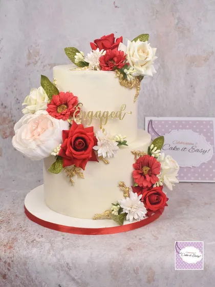 A classic two-tier engagement cake with a cascade of red and white flowers and subtle gold accents.