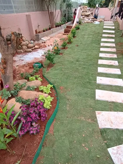 The finished backyard garden, featuring a vibrant new lawn, a clean stone pathway, and colorful planting beds along the border.
