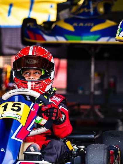 A young driver in his red race suit, looking focused in his kart.