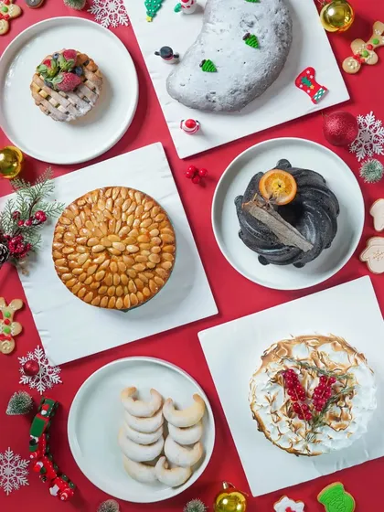 A flatlay of various Christmas cakes and cookies on a bright red background. This top-down shot is a vibrant and festive showcase of a bakery's holiday offerings.