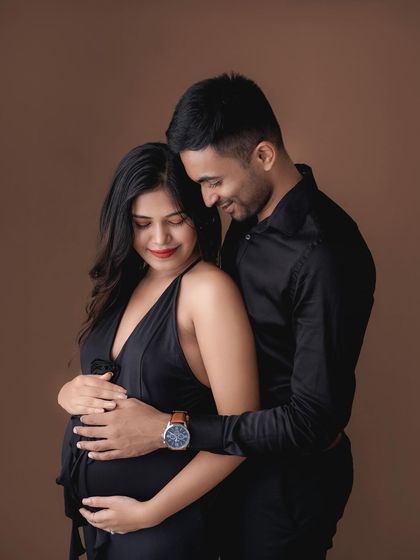 An intimate embrace during a studio maternity session. The dark clothing and background create a moody and romantic feel.