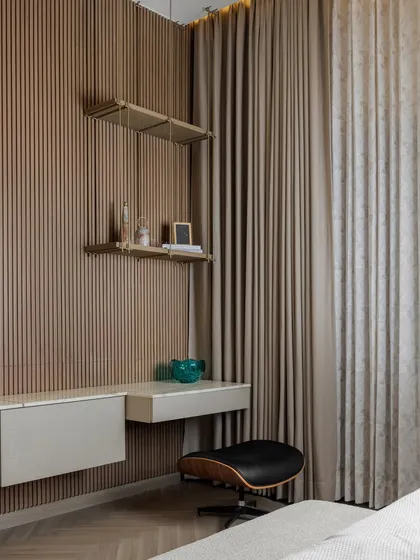 The study corner in the daughter's bedroom includes a floating desk and a stylish chair. The wall is clad in vertical wood fluting, adding warmth and texture to this functional nook.