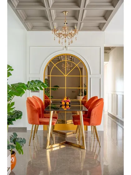 The dining area is defined by bold, burnt-orange velvet chairs and a striking gold-framed arch mirror. This combination creates a focal point that is both dramatic and sophisticated.