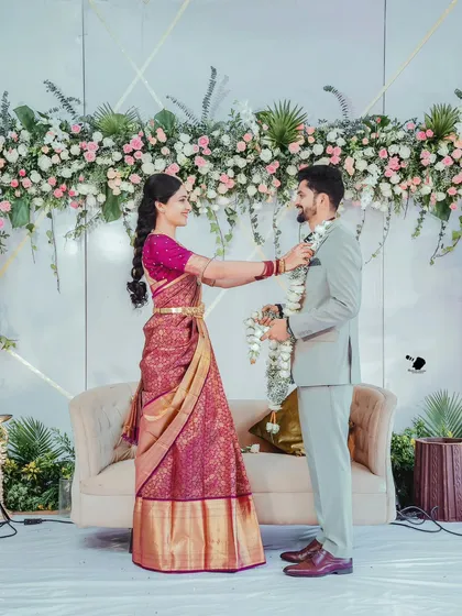 A beautiful moment from Sanchitha and Vinay's ceremony. The backdrop features a dense arrangement of pink and white roses with cascading greenery, perfectly framing the couple as they exchange garlands.