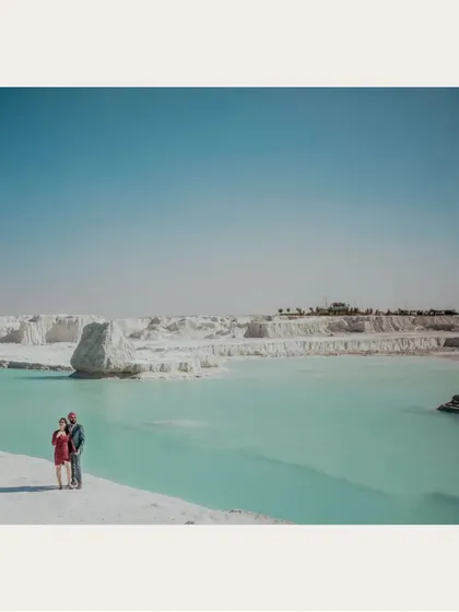 A wide shot of a couple standing by a turquoise lake in a surreal white landscape. This location provides a unique and unforgettable backdrop for pre-wedding photos.