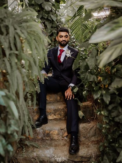 A handsome portrait of the groom seated on stone steps in a garden, looking sharp in his suit.
