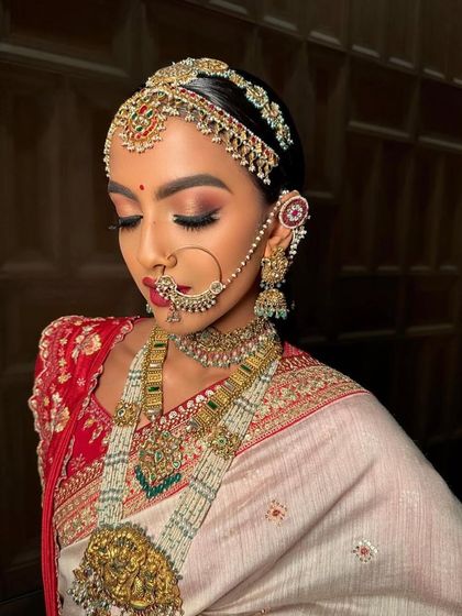 A close-up of a traditional South Indian bride with a modern twist. The makeup features a bold red lip and dramatic eyes, paired with stunning temple jewellery.