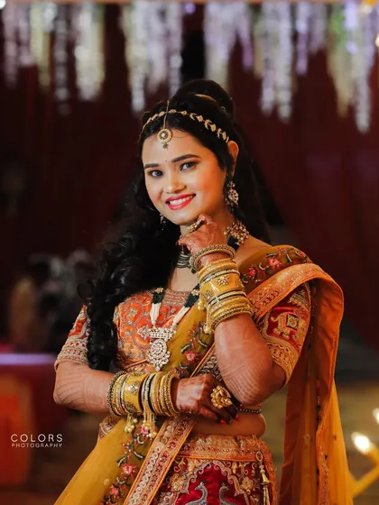 A vibrant portrait of a bride in a traditional mustard and red lehenga, smiling brightly for the camera.