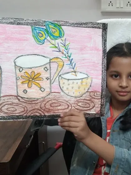 Neev, a 2nd standard student, with his still life drawing. He has used oil pastels to draw a collection of cups and a vase with peacock feathers.