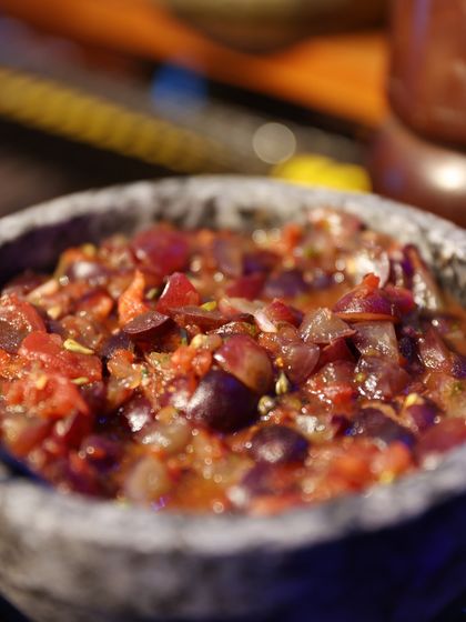 A rustic stone bowl filled with a chunky grape and tomato salsa, a unique and flavourful accompaniment to our dishes.