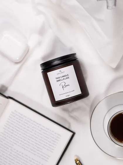 A cozy, "morning in bed" flat lay featuring a Delight Candle. The styling with a book, coffee, and AirPods creates a relatable, relaxing lifestyle scene.