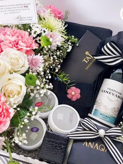The epitome of regal romance. This luxury hamper includes a bottle of wine, gourmet treats from Anaqi, and Taj Experiences vouchers, all nestled in a bed of fresh pink and white carnations.