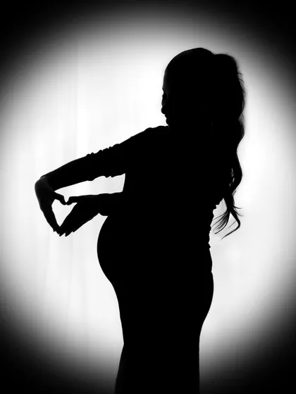 A beautiful silhouette of a mother-to-be making a heart shape over her bump. The spotlight effect creates a dramatic and emotional focus.