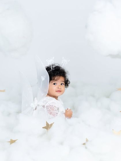 A quiet, thoughtful moment for our little angel among the clouds. The soft lighting and dreamy setting create a serene and beautiful portrait.