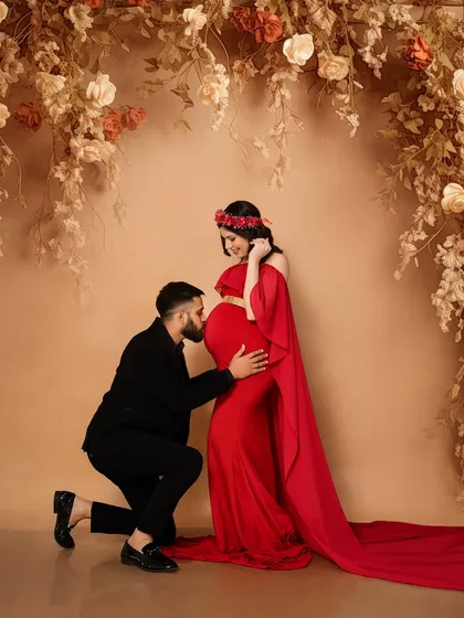 A dramatic and elegant maternity portrait. The striking contrast of the flowing red gown against a fine art, neutral-toned backdrop creates a powerful, celebratory image. This style is perfect for parents who want a bold and artistic commemoration of their pregnancy journey.