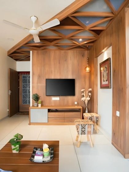 This living room showcases our expertise in using wood for both wall paneling and a unique geometric false ceiling design. The integrated TV unit maintains the room's cohesive and warm aesthetic.