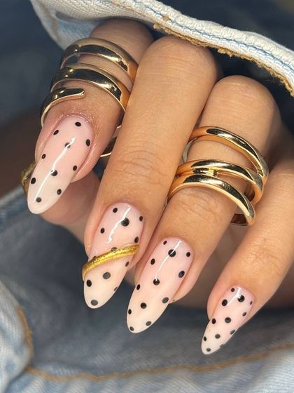 A chic and fashionable polka dot manicure on long, stiletto nails. The look is elevated with a sculpted gold ring accent, blending nail art with jewelry.