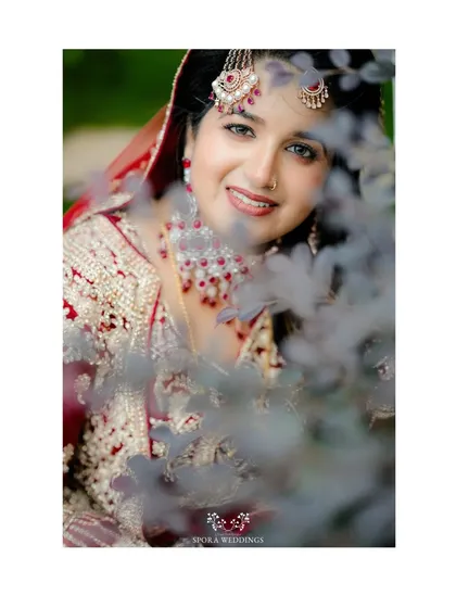 A lovely close-up of the bride, her smile peeking through the leaves, showcasing her intricate jewelry.