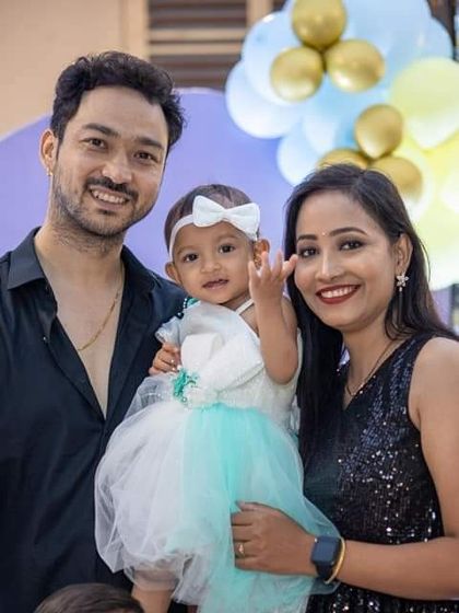 A happy family portrait from a first birthday party. The baby girl, dressed in a cute party dress, is the center of attention.