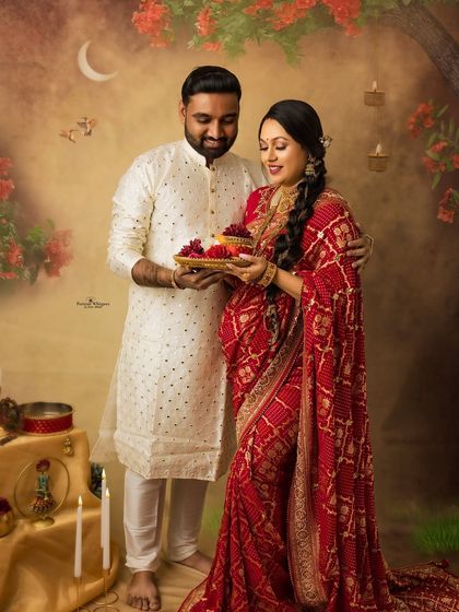 A classic Karva Chauth portrait of a couple. The husband holds the offering plate as they share a loving moment, celebrating their bond and the new life they are awaiting.