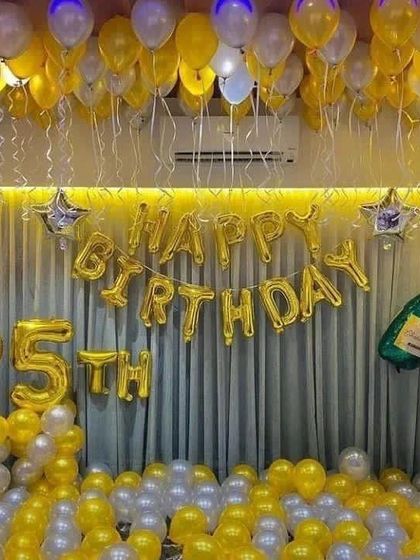 A 25th birthday room decoration with gold and silver balloons covering the floor and ceiling, with large foil numbers and a champagne bottle accent.
