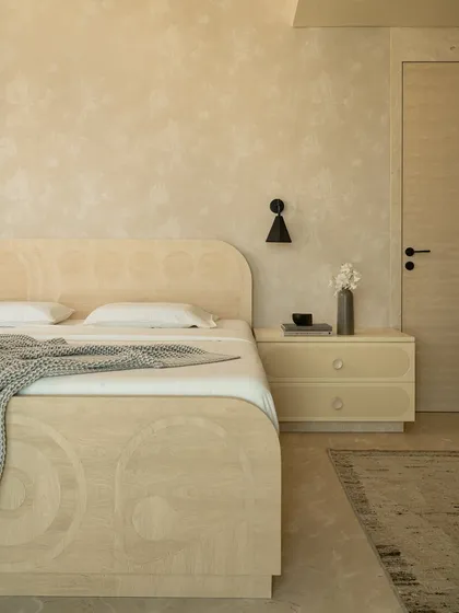 The master suite in the 'Soft Serve' project is enveloped in a timeless taupe. The custom bed and vanity feature abstract patterns in Movingue White veneer, with scalloped motifs framing the bay window.