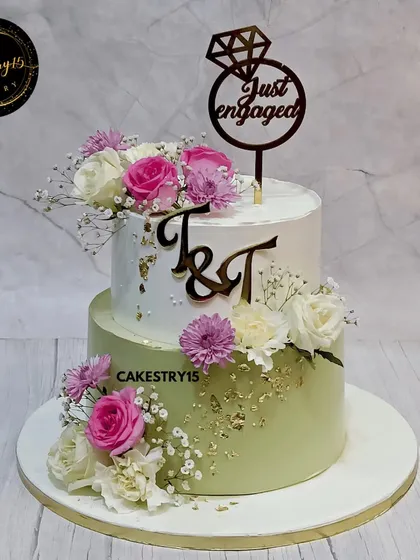 A beautiful two-tier engagement cake combining Black Forest and Butterscotch flavors. This 5kg creation is decorated with fresh pink and white carnations, gold leaf, and a custom initial topper.