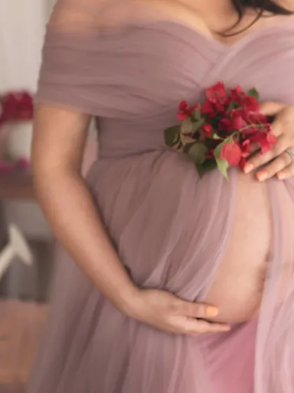 A close-up detail shot focusing on the baby bump, draped in soft tulle. The addition of fresh bougainvillea flowers adds a pop of color and a touch of natural beauty.