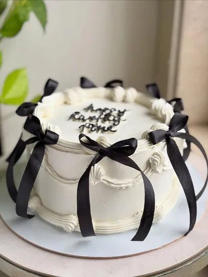 The full view of the balletcore-inspired cake, showing how the black ribbons create a dramatic and chic contrast against the soft white buttercream.