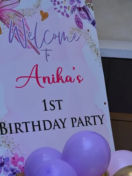 A close-up of a welcome sign for a butterfly-themed first birthday party, featuring a delicate purple and pink floral design.
