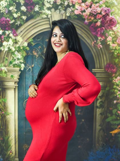 A fun and happy portrait of a mom-to-be in a bright red dress, smiling in front of our floral studio backdrop.